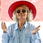 Joyful senior woman wearing a vibrant red hat and sunglasses, expressing happiness outdoors.