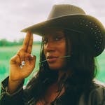 Stylish woman wearing a cowboy hat in a green field.